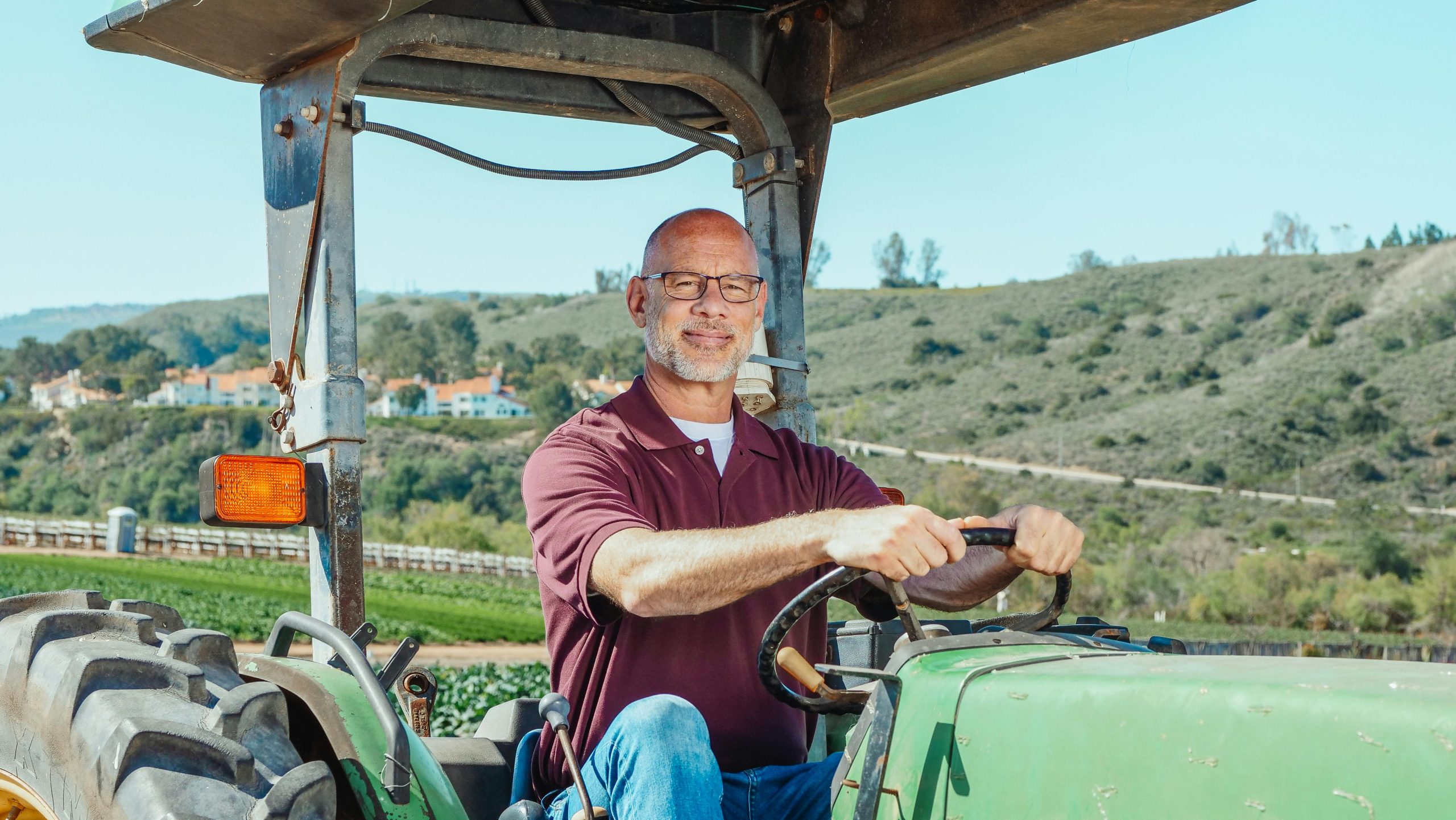 Elderly man on a tractor in a scenic rural landscape, enjoying farm life.